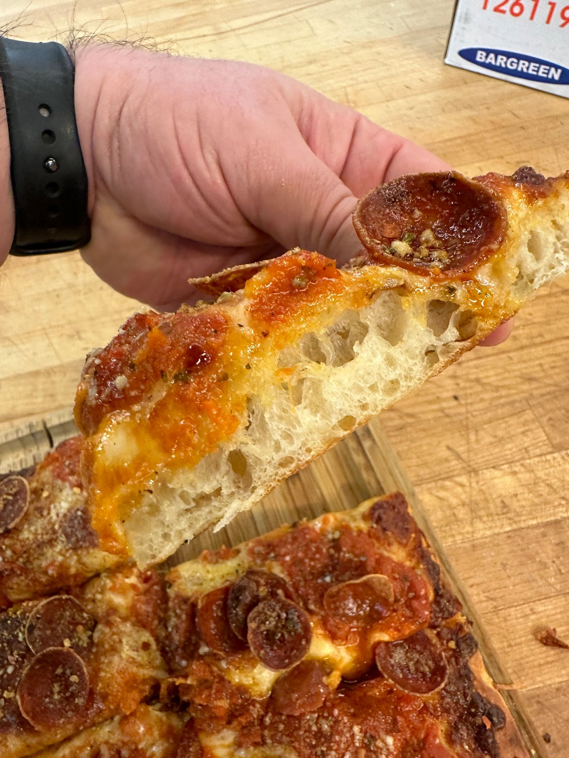 Slice of Detroit pizza held up showing the airy crumb