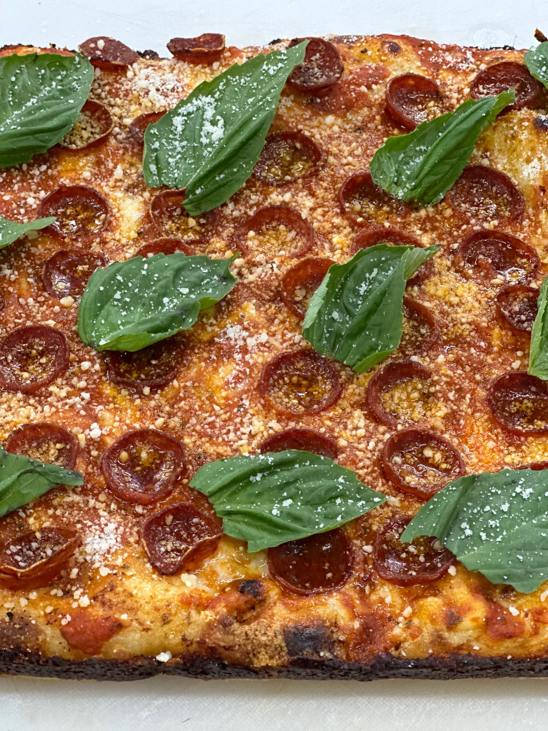 Detroit-style pepperoni square topped with fresh basil leaves and grated parmesan.